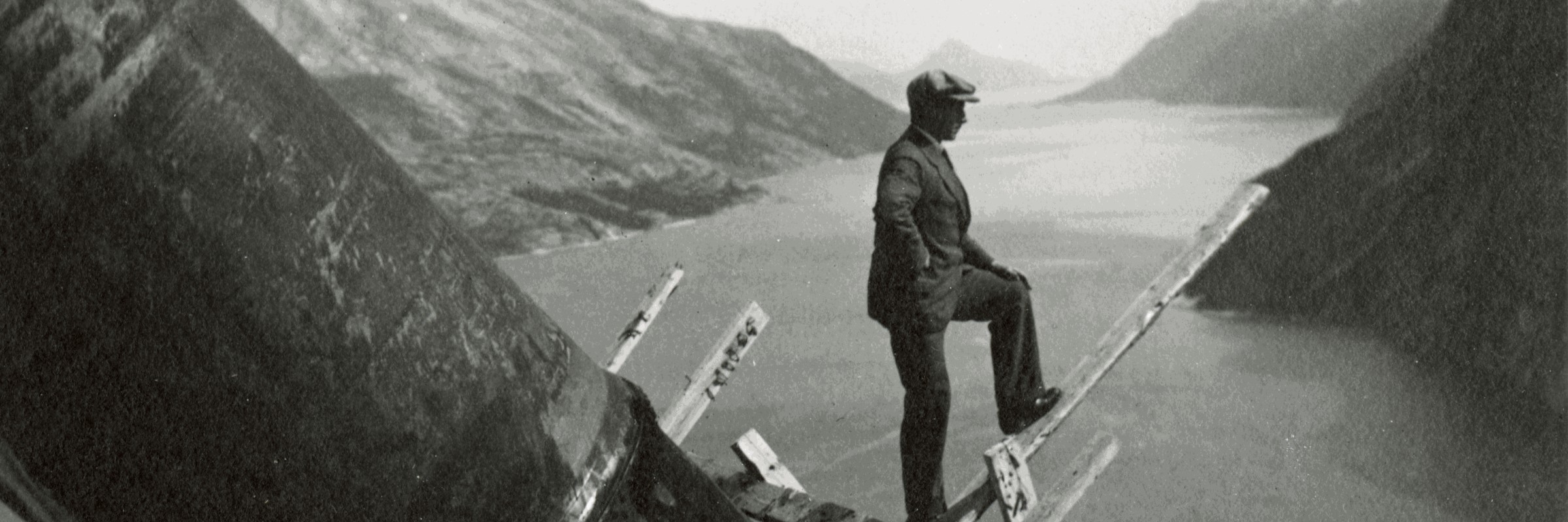Black and white image of man looking out over a fjord